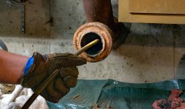 Hands of a plumber as he runs a camera scope and cleaning machine through the main pipe to unclog the drain to the Septic System. Hard-working tradesman.